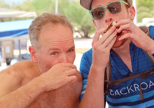 Two guests eating oysters, boats behind them.