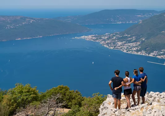 Four guests, arms around each other on hilltop, overlooking ocean vista.
