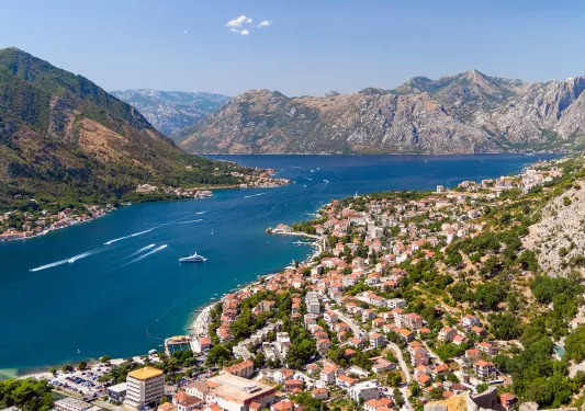 Bird's eye of Croatian riverside city, mountains all around, boats in river.