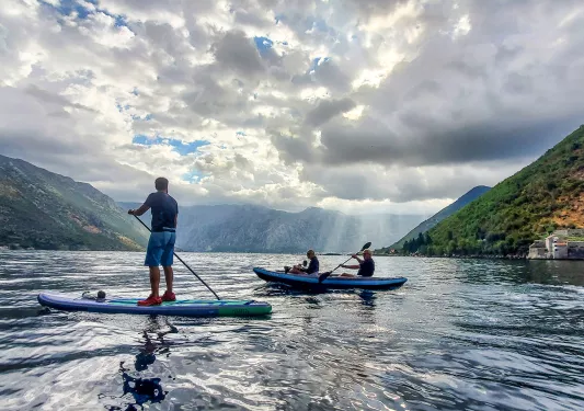 Two guests kayaking, one paddle boarding, clouds, hills in distance.