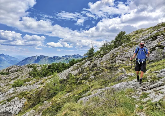 Guest hiking on craggy hillside, cloudy sky behind them.