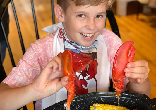 Young guest eating lobster, holding up both claws.