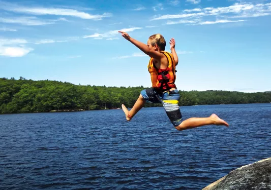 Young guest jumping from rock into lake.
