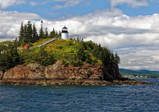 Wide shot of small island, white lighthouse and small red building on it.