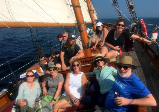 Group of guests on tilting sailboat, all facing camera.