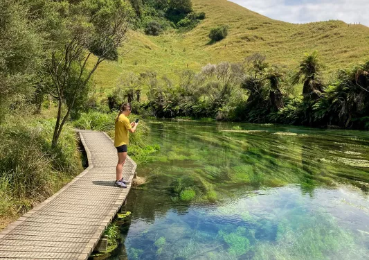Guest on small bridge, taking photo of clear lake.