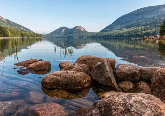 Wide shot of reflective lake, rounded mountains.