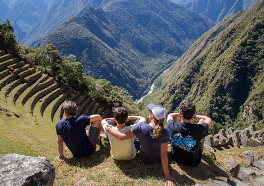 Four guests sitting on Machu Picchu hillside, overlooking mountains. 