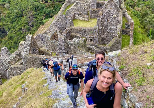 Guests hiking up stone trail, Machu Picchu ruins behind them.