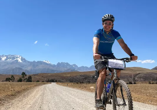 Guest cycling down dirt trail, hilly vista, mountain, blue sky.