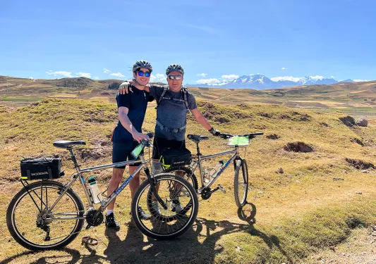 Two guests with bikes on golden meadow, mountains behind them.