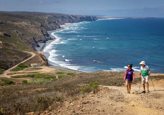 Two hikers walking up a sandy hill with the ocean in the background