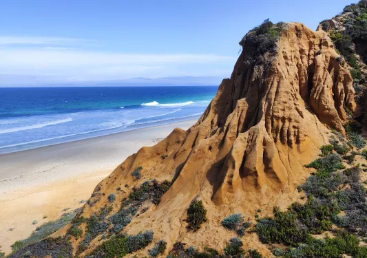 Hillside shot of sandy cliff, beach, ocean below.