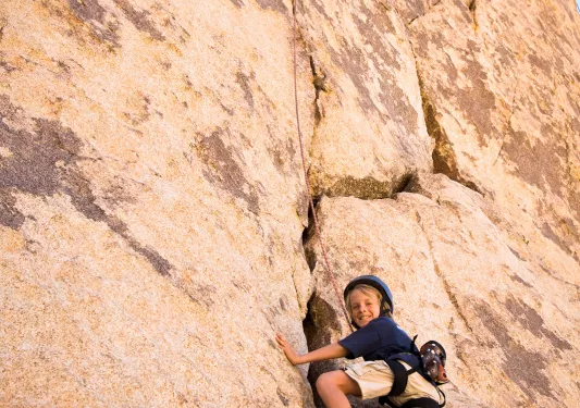 Child rock climbing on sandy cliffside.