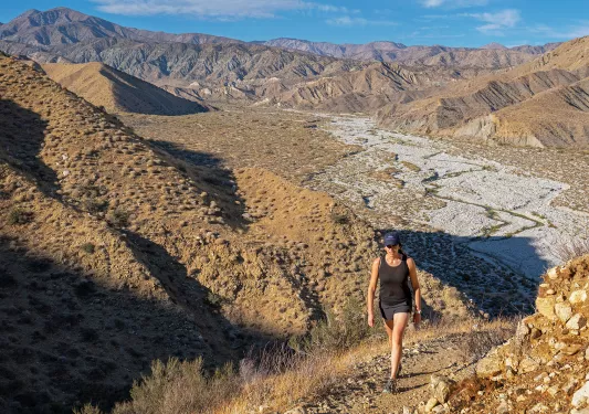 A woman hiking up a hill in the desert with mountains in the background