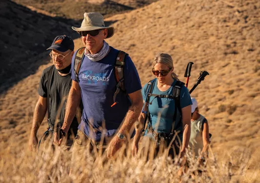 Four guests hiking up hill, surrounded by yellow grass and hills.