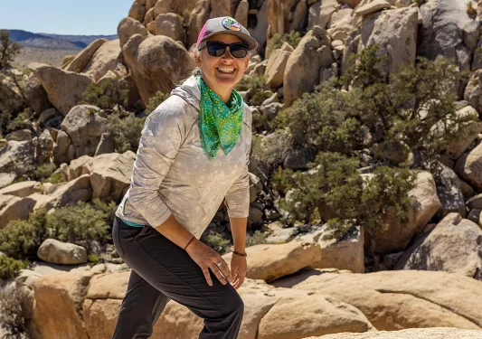 Guest hiking up desert boulder, craggy sandstone rocks in background.