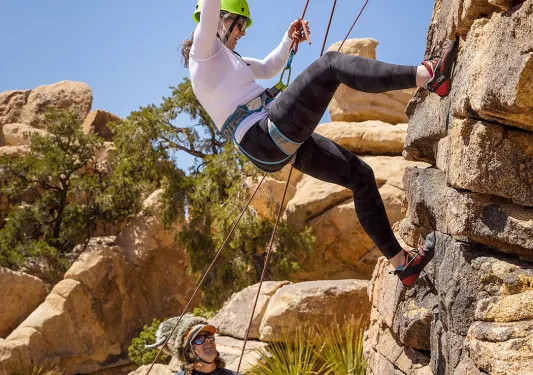 Three guests rock climbing, one is waving to the camera.