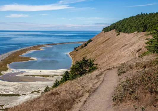 Wide shot of brown, dirt cliffside, small pools, ocean in distance.