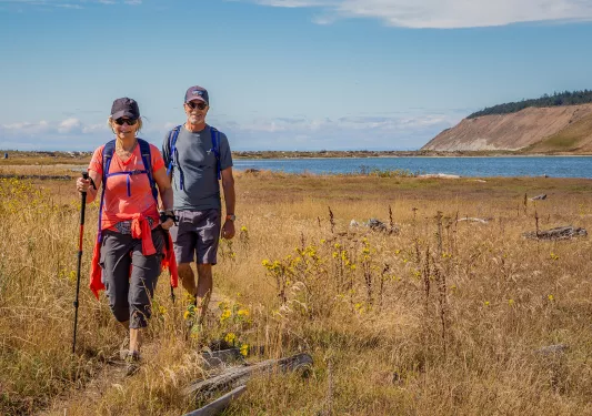Two guests walking through grassy coast, ocean, cliffside behind them.