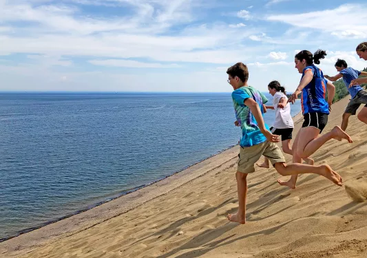 Group of young guests running down sand dune towards ocean.
