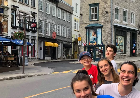 Group of young guests in foreground, grey brick buildings and alleyways in background.