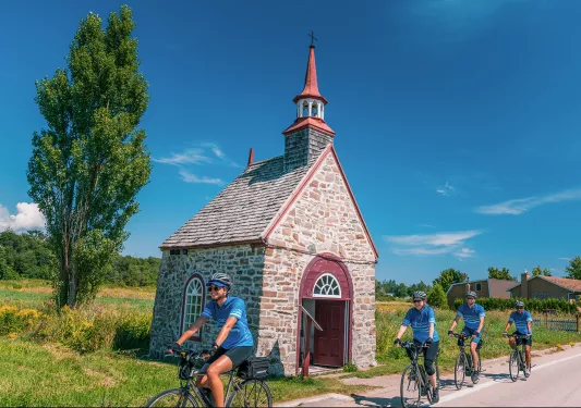 Four guests cycling past small brick building.
