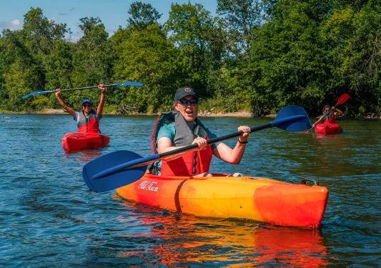 three guests kayaking, one is celebrating in background.