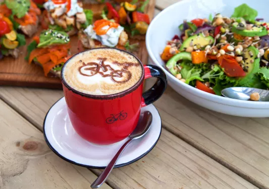 Table with platters of food and a cappuccino with a bicycle drawn in the foam