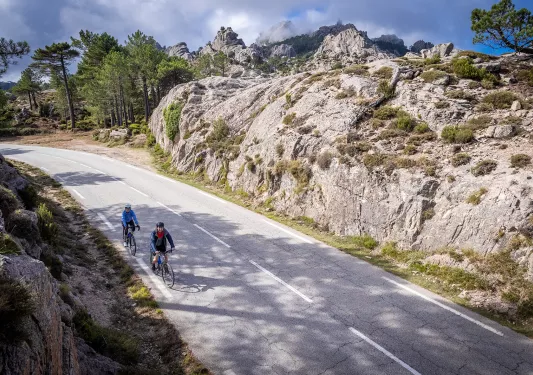 Two guests cycling down road, between large, craggy rock faces.