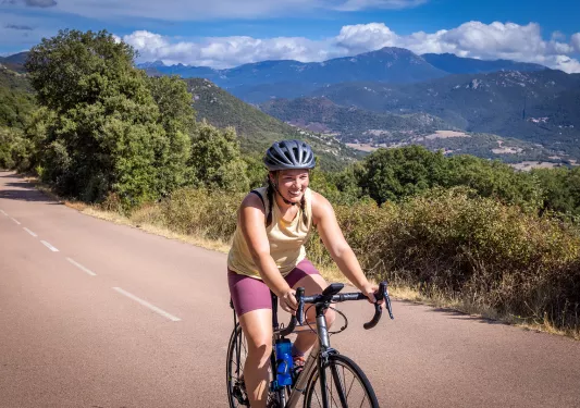 Guest cycling down road, hills and mountains in background.