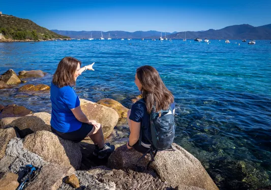 Two guests sitting on large rocks on coast, one pointing towards ocean.