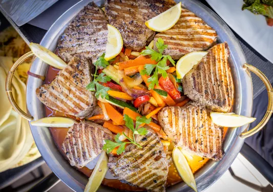 Platter of food, grilled meat, veggies, lemon slices, etc.