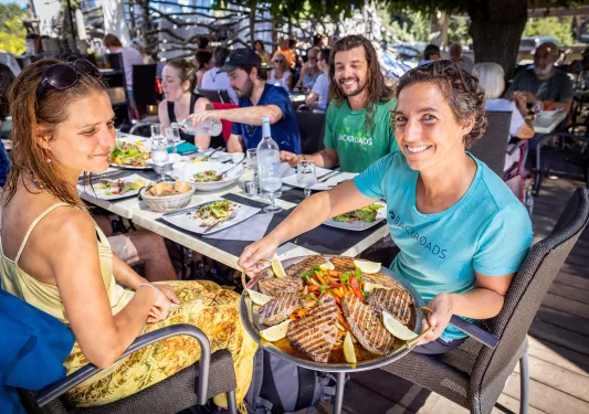 Group of guests at dinner, One is holding a platter of seared meats and veggies.