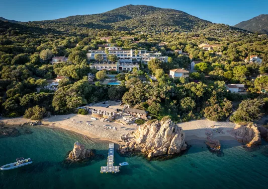 Wide shot of a large hotel in the hillside, beach, small boats and ocean in foreground.