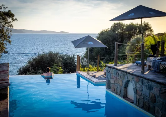 Guest relaxing in a pool, overlooking ocean and distant hills.