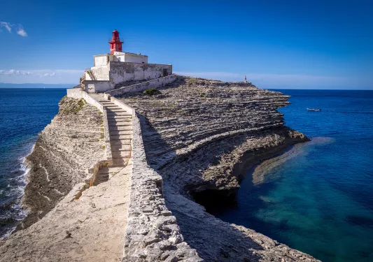 Point of view shot of a rocky trail leading towards a small lighthouse.