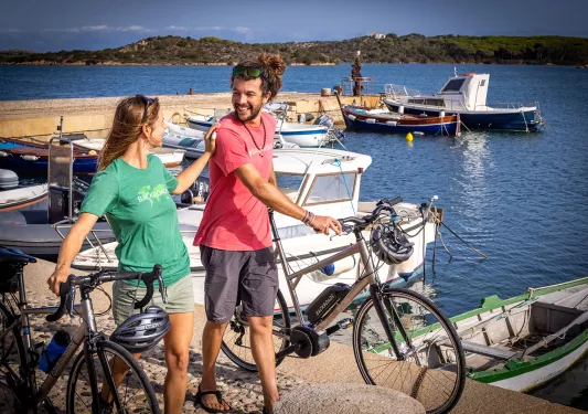 Two guests with bikes, walking along pier, boats around them.