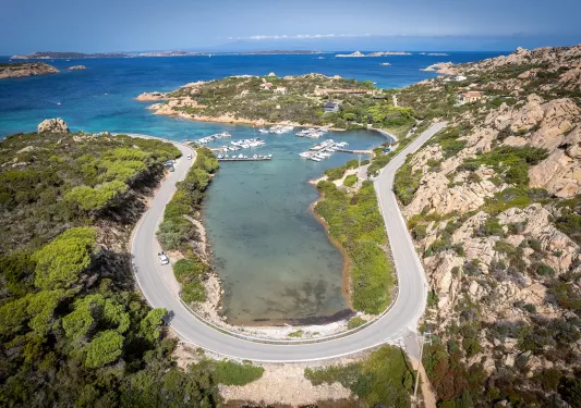 Bird's eye shot of a "U" shaped road on the Italian coastline, small boats and piers in distance.