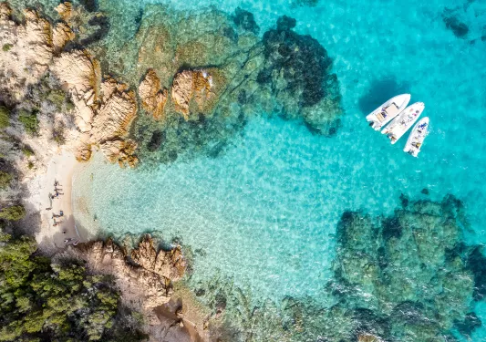 Overhead shot of guests on the beach, some are on small boats in the water.