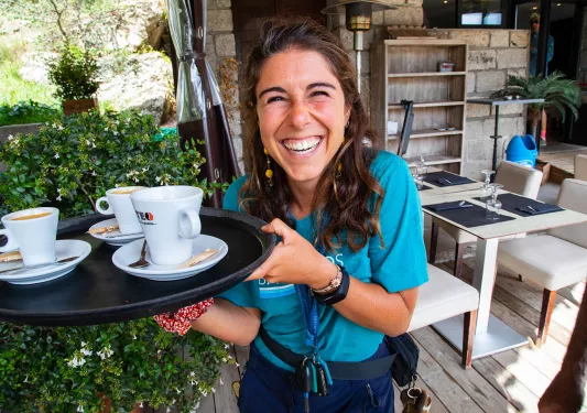 Leader smiling at camera, holding platter with three coffee mugs.