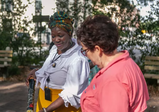Two women talking, one is showing the other a tube-like object.