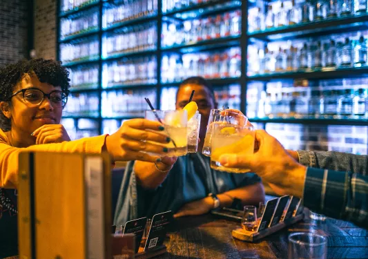 Four guests at a bar, cheersing cocktails.