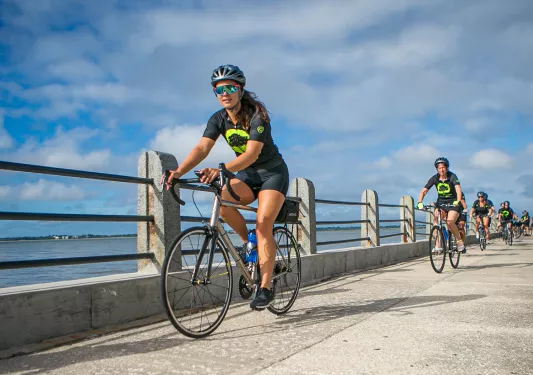 Group of guests riding past ocean next to stone/metal fence.