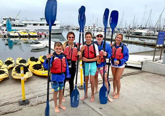 Five guests getting ready to kayak, oars in hand.