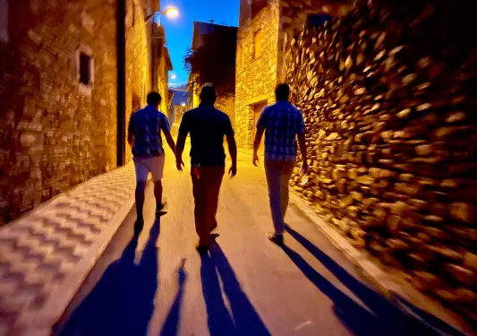 3 men walking down the street at night with streetlight causing long shadows