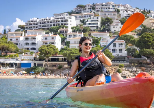 Woman kayaking in turquoise waters with white buildings in the background
