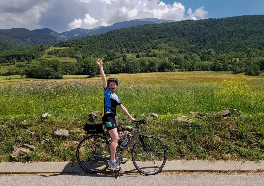 Backroads guest waving at the camera while riding her bike past a green field