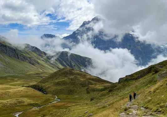 Wide shot of mountainous vista, two guests in distance.