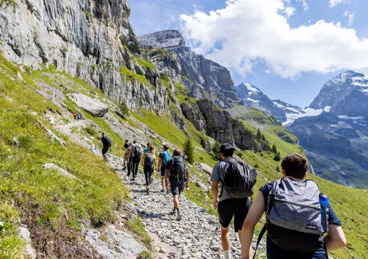 Line of guests on rocky cliffside, mountains ahead.